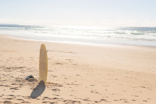 Yellow surfboard standing in sand on Atlantic beach. Caparica, Lisbon, Portugal. 2 December 2023.