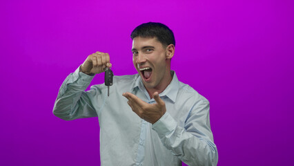 Man holds car key and pumps fist in purple studio setting, smiling broadly while displaying keys;...