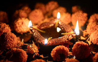 Deepavali or Diwali Festival Clay Diya with Oil and Glowing Flames with Marigold Flower Petals on Black Background with Copy Space, Happy Diwali or Deepavali Festival Celebration Concept