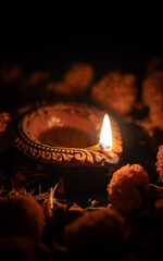 Closeup of Deepavali or Diwali Festival Traditional Clay Oil Diya and Glowing Flame with Marigold Flower Petals on Black Background with Copy Space, Happy Diwali or Deepavali Festival Concept