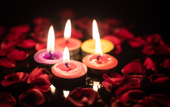 Closeup of Diwali Candles with Glowing Flames with Red Rose Flowers Petals on Glossy Black Background with Copy Space, Happy Diwali or Deepavali, Festival of Lights, Romantic  Date Concept