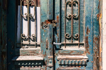 Close-up of weathered blue wooden doors with rusted metal details and old padlock. Texture of peeling paint reveals aged craftsmanship, symbolizing history, decay, and urban charm.