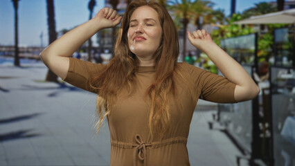 Woman in brown dress covers mouth yawning on busy sunlit street lined with palm trees under clear blue sky; fatigue.