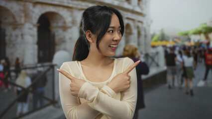 Fototapeta premium Young chinese woman smiling and pointing at both sides outside the roman coliseum, showcasing a lively outdoor scene in rome's iconic architecture.