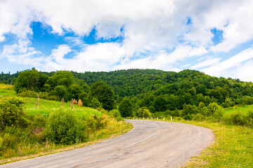 uzhanian pass in carpathian mountain landscape. old asphalt country road take turn downhill near forest. rural scene with field and haystacks in summer under cloudy sky. countryside travel background