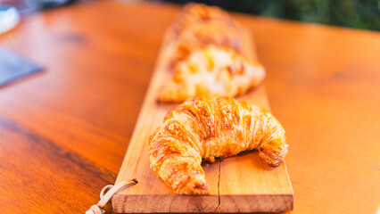 Beautifully presented golden brown, crispy croissants on a wooden board, fresh from the oven and ready to eat. Perfect for bakery promotions and breakfast menus.