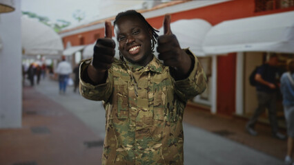 Young man soldier in camouflage uniform gives thumbs up on a busy street lined with white awnings...