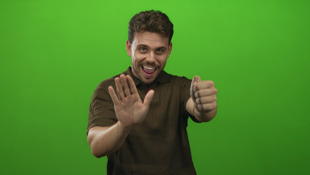 Man with hands gripping an imaginary steering wheel in a green studio, wearing brown polo shirt and focused expression; confidence driver roleplay.