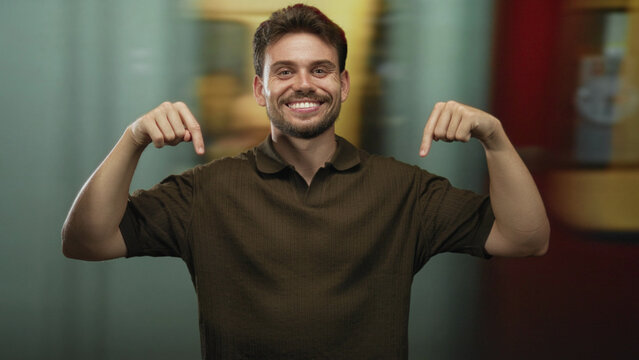 Man points both index fingers downward at train station platform, smiling and gesturing to space below; friendly invitation.