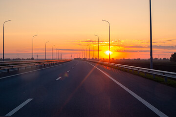 A view of a highway at dusk at sunset. A smooth strip of highway devoid of traffic