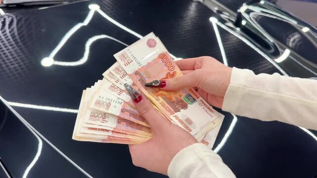 In the girl's hands counts a bundle of bills for five thousand Russian rubles. Girl counts red paper 5000 rubles bills. Russian cash money in female hand. A girl holds a wad of money in his hands.