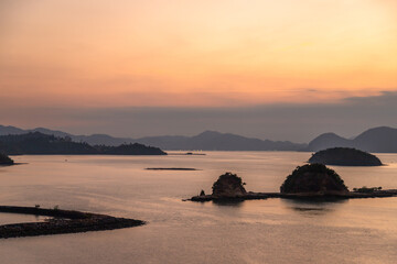 Tranquil view of small tropical islets silhouetted at sunset near Langkawi port, Malaysia. The soft pastel sky reflects on calm sea waters, creating a peaceful and scenic landscape perfect for travel