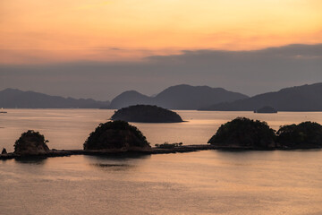 Tranquil view of small tropical islets silhouetted at sunset near Langkawi port, Malaysia. The soft pastel sky reflects on calm sea waters, creating a peaceful and scenic landscape perfect for travel