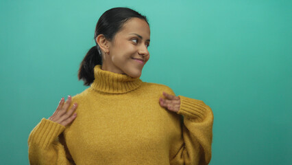 Woman smiling in a mustard sweater against a green background, exuding confidence and warmth with an isolated, youthful, hispanic charm and casual style.