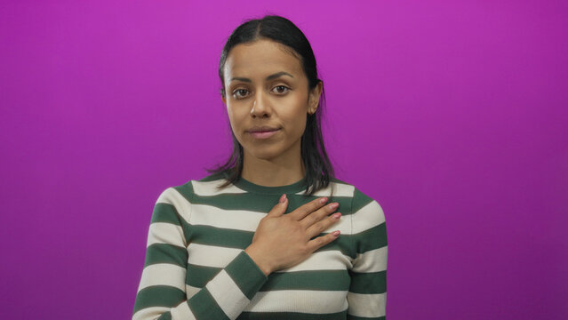 Young hispanic woman making pledge gesture against isolated pink background wall, wearing striped sweater, expressing serious commitment and solemn promise.