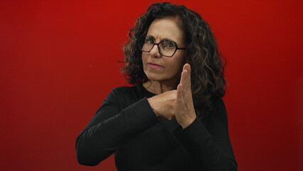 Middle aged hispanic woman holds up bare fists in a studio against a red wall; defiance determination strength.