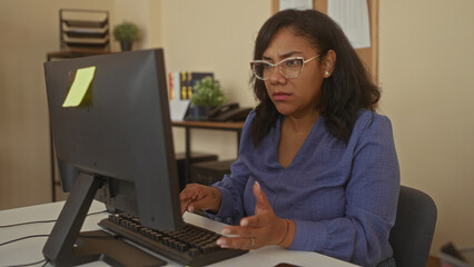 Woman types on computer keyboard in office building at desk with a yellow sticky note on the...