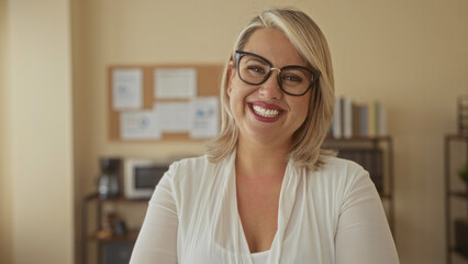 Woman with glasses smiles broadly and looks at camera in office building; confidence optimism...
