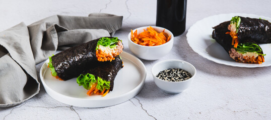Tuna, cheese, Korean carrots and lettuce wrapped in nori on a plate on the table web banner