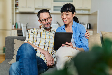 Portrait of a lovely young couple using a tablet computer together and having fun sitting on sofa at home