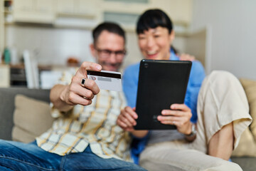 Portrait of a lovely young couple using a tablet computer and online shopping holding credit card together and having fun sitting on sofa at home