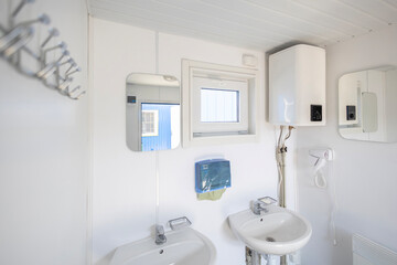 A clean, functional washroom in a modular cabin, equipped with twin sinks and an electric water heater. The practical setup provides essential hygiene amenities for workers in a temporary housing unit