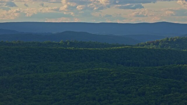 Scenic view from Lina Constable Overlook of West Virginia's Lost River Valley. Layers of lush, green forested mountains recede into a blue haze under a partly cloudy sky.