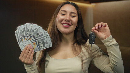 Woman smiles and holds fan of cash and lifts car key in studio; success wealth prosperity...
