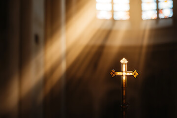 Naklejka premium Golden cross bathed in sunlight, stained glass windows filtering light, creating a spiritual ambiance. Symbol of faith and hope in a tranquil church setting.