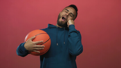 Man holding basketball and resting head on hand while yawning in a pink studio; sleepy rest solitude.