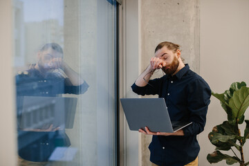 Stressed businessman rubbing eyes holding laptop