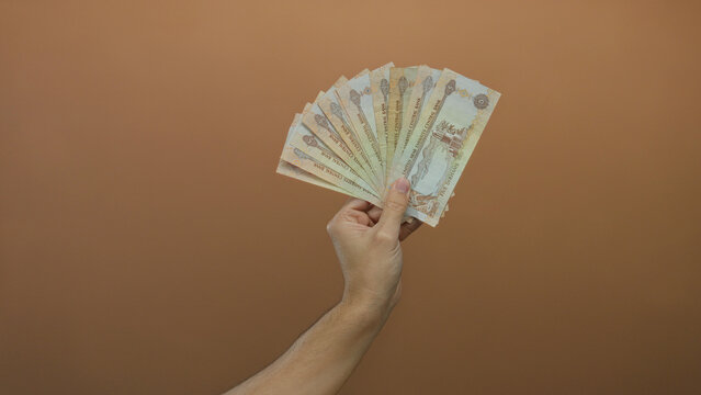 Hand holding uae dirham banknotes against a brown wall, depicting a caucasian male with an isolated money display.