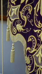 Detailed church tapestry with intricate gold embroidery and tassels hanging indoors, displaying elaborate religious motifs on rich purple fabric.