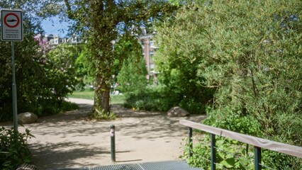 Blurred park scene with green foliage, bokeh background, and defocused trees under sunlight in a peaceful urban setting.