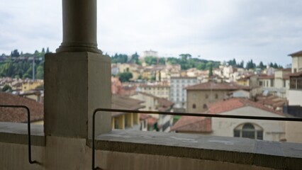 Balcony foreground pillar and stone railing in sharp focus with terracotta roofline and distant buildings softly blurred city; background backdrop copyspace.
