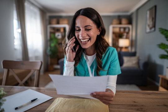 Female nurse laughing during phone call reading paperwork at home - Powered by Adobe
