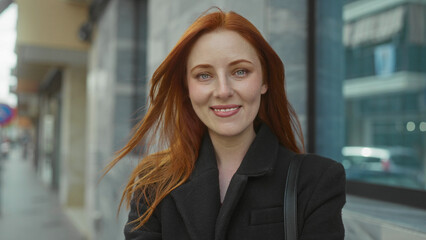 Fototapeta premium Woman with red hair confidently standing outdoors in city street, showcasing an engaging expression that reflects urban charm.