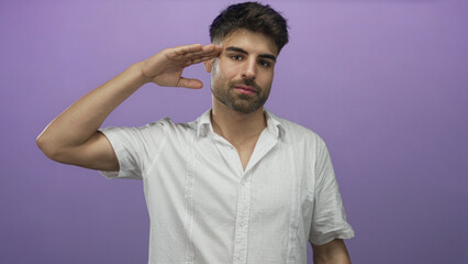 Hispanic man in white shirt lifts bare hand to forehead in a purple studio setting saluting with...