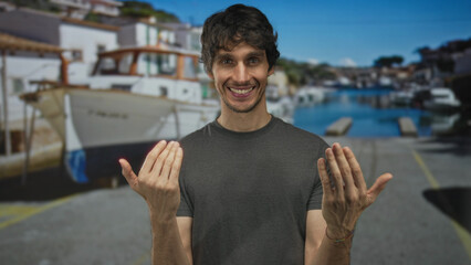 Man shows both palms gesture on sunlit street dock near white boats under blue sky; warm invitation.