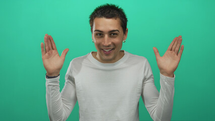 Young man wearing white shirt covers eyes with hands then lowers hands and smiles in studio;...