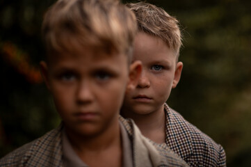 Close portrait of two serious boys, one standing behind the other. Focus on eye, blurred front face. Concept of childhood, identity, and emotional connection.