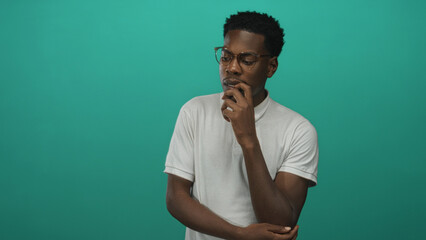 Man with finger on chin gesture in green studio, wearing eyeglasses and white polo shirt;...