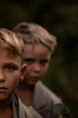 Close portrait of two serious boys, one standing behind the other. Focus on front eye, blurred background face. Concept of childhood, identity, and emotional connection.