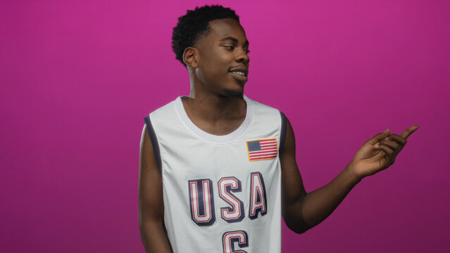 Man wearing usa basketball jersey pointing finger in pink studio; confidence patriotism youth optimism.