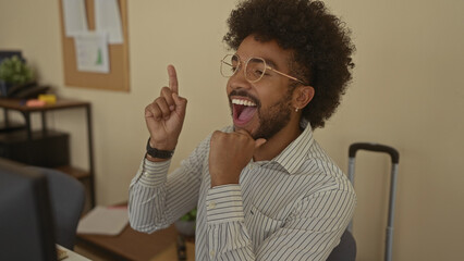 Man in an office with an idea, wearing glasses and a striped shirt, gesturing excitement in a professional indoor setting, conveying creativity and innovation.