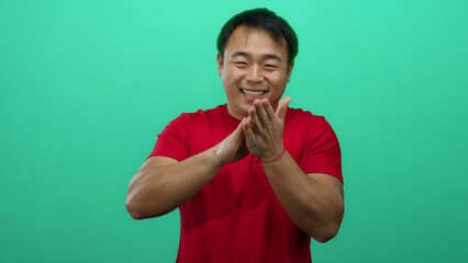 Young man in red shirt making money gesture against green background with a cheerful expression...