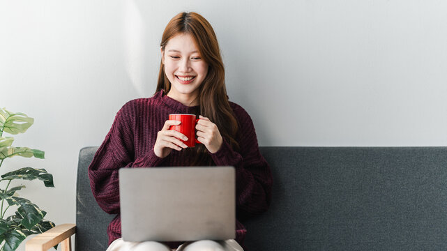 Young Asian Woman Enjoying Coffee Break with Laptop on Couch Relaxing with Hot Drink