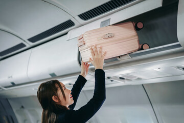 traveler stows pink luggage airplane overhead bin cabin storage compartment flight travel journey passenger aircraft trip vacation business suitcase smiling person