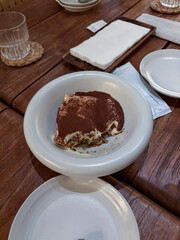 Tasty tiramisu dessert half eaten on a white plate served in a restaurant