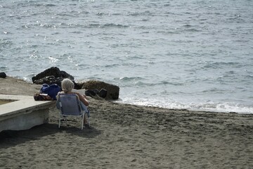 Ostia, Rome, Italy - October 19, 2025, a lady from behind sunbathes on the beach on a folding chair on a beautiful October day, called ottobrate romane in Rome.